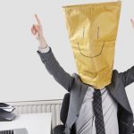 Businessman cheering with smiley drawn on paper bag over face in office